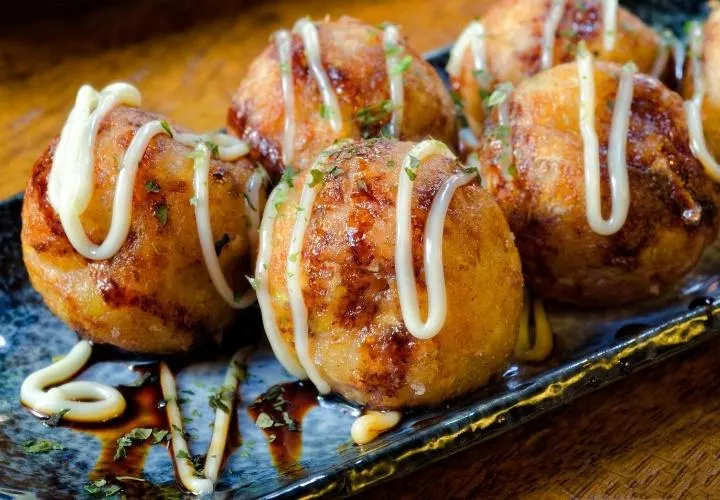 Vegan takoyaki balls topped with sauce, vegan mayo and spring onion on a plate