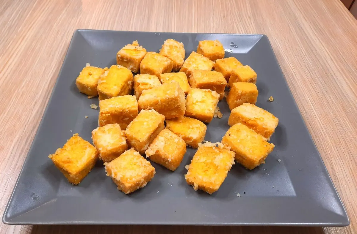 Golden puffed tofu cubes draining on paper towel after frying