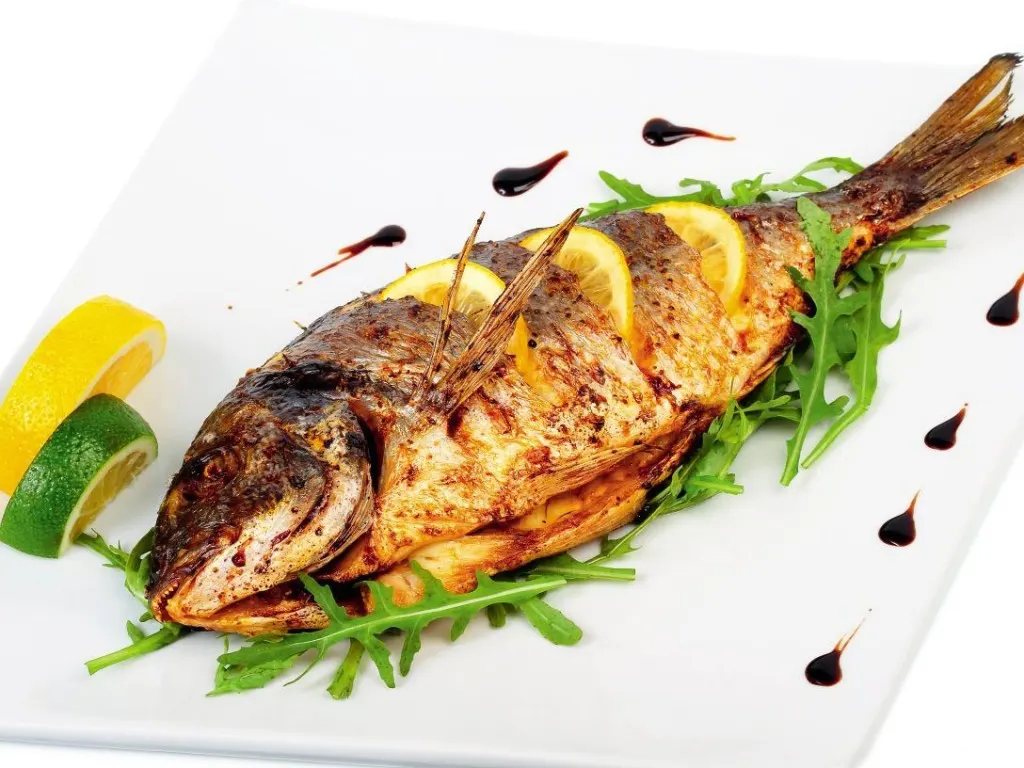 A whole fresh croaker fish on ice, showing its silver skin and firm flesh
