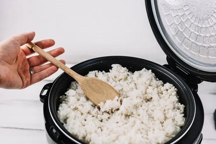 A pot of cooked white rice being fluffed with a fork