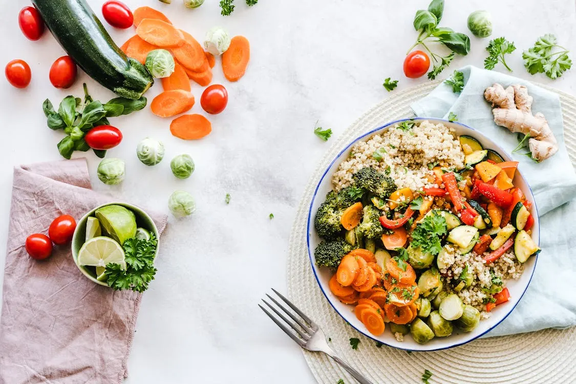 A colourful plate filled with assorted vegetables and rice, accompanied by a fork and spoon on the side.