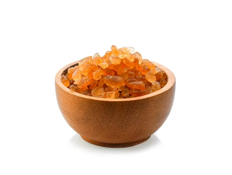 A wooden bowl filled with peach gums, placed on a wooden surface. The peach gum pieces are large, crystalline, and have a slightly translucent appearance, highlighting their texture and natural beauty.