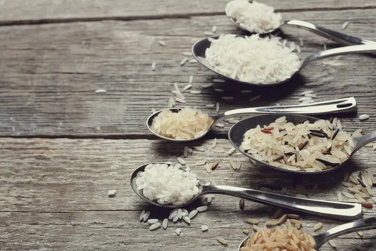 An assortment of various types of rice displayed on a wooden table. The different grains, including white, brown, and wild rice, highlight the diversity in texture and colour.