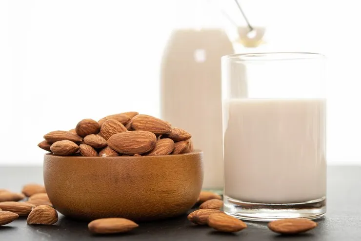 Almonds and a glass of almond milk beside a bowl of cereal on a rustic table, ideal for a nutritious meal.