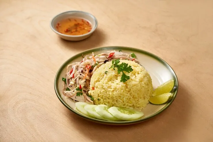 A plate of crispy rice salad with vegetables, garnished with chili garlic paste, set on a rustic wooden table.