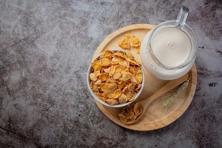 Cereals and vegan milk are presented on a wooden plate, with a grey backdrop, showcasing a delicious non-dairy breakfast.