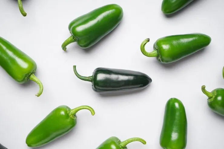 A pile of fresh green jalapeño peppers on a white background, shot from above