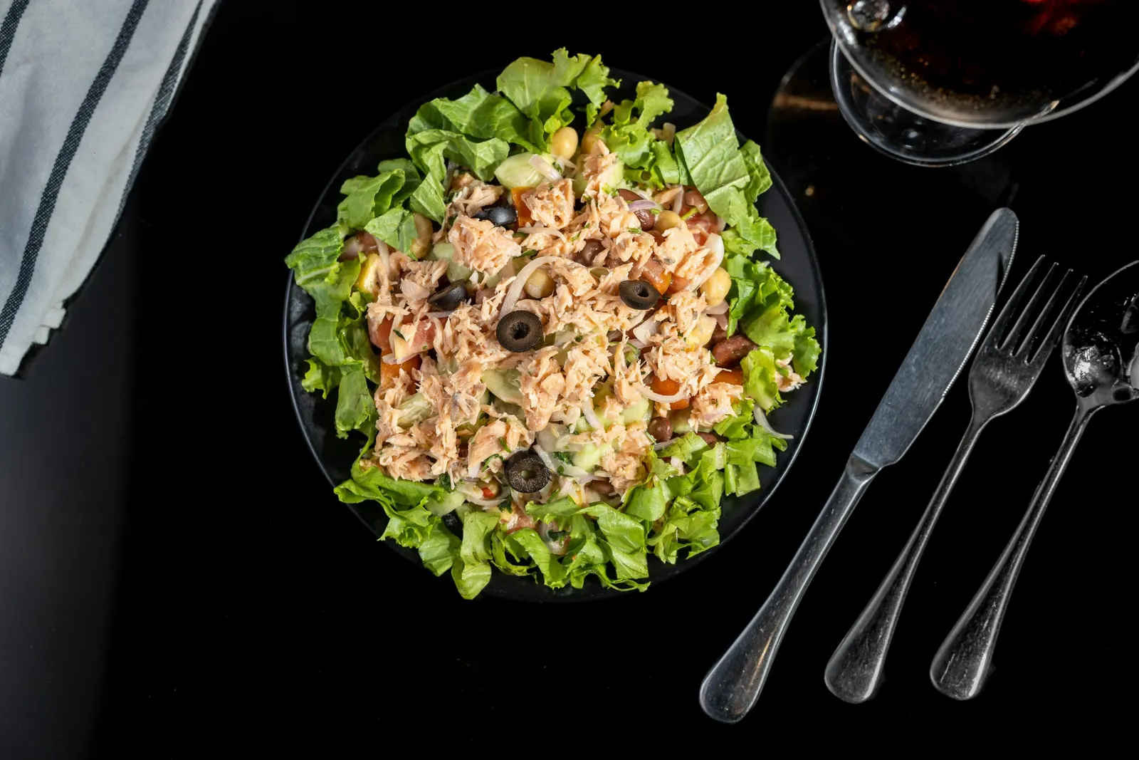 A vibrant plate of salad featuring grilled chicken, olives, and fresh vegetables, showcasing a healthy meal option.