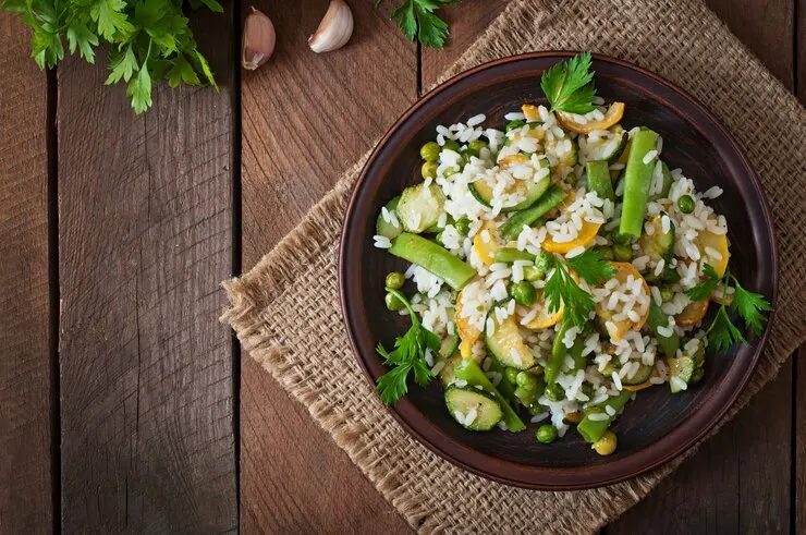 A vibrant crispy rice salad featuring asparagus, peas, and carrots, beautifully arranged on a rustic wooden table.