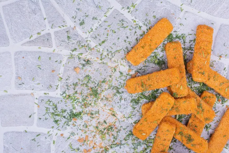 A pile of vibrant cheesy vegan mozzarella sticks arranged neatly on a white background, perfect for a healthy Valentine's Day treat. 
