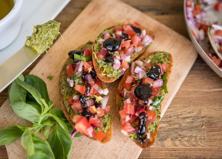 Baked bread topped with pesto and olives, perfect for a romantic vegan bruschetta on Valentine's Day. 
