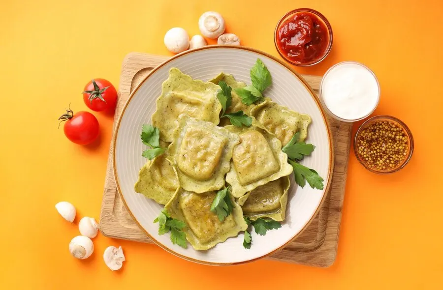 A plate of vegan kale and sweet potato ravioli topped with colourful vegetables and a rich sauce, perfect for Valentine's Day.