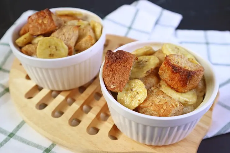 Fresh baked mouthwatering banana bread pudding ceramic bowls wooden breadboard