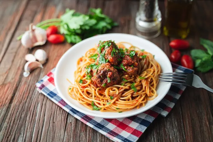  A plate of vegan spaghetti topped with lentil balls and tomato sauce, elegantly presented on a wooden table for Valentine's dinner.