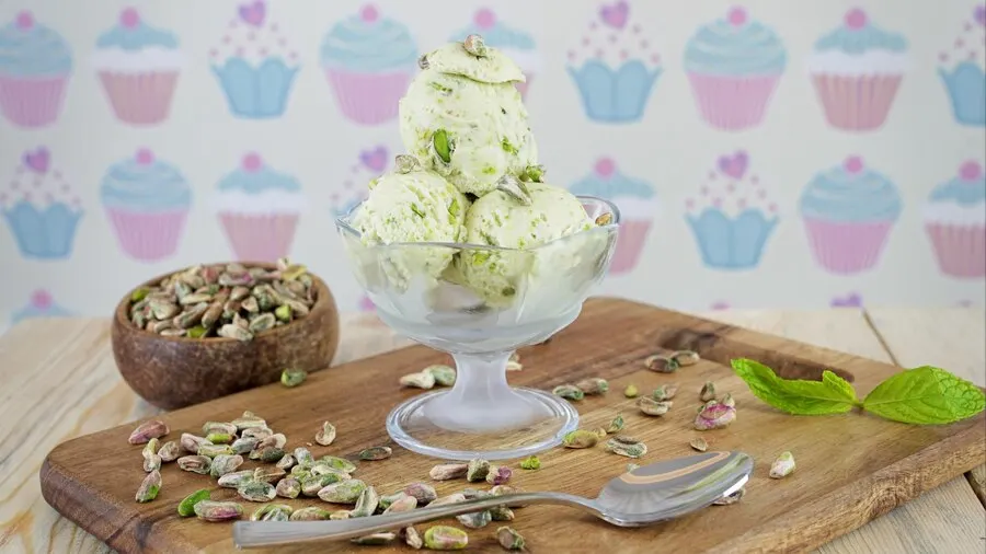 A bowl of vegan pistachio ice cream topped with pistachios and fresh mint leaves, showcasing a vibrant green colour.