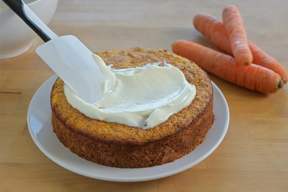 Vegan carrot cake topped with smooth cream cheese frosting, showcasing a moist texture and vibrant orange colour.