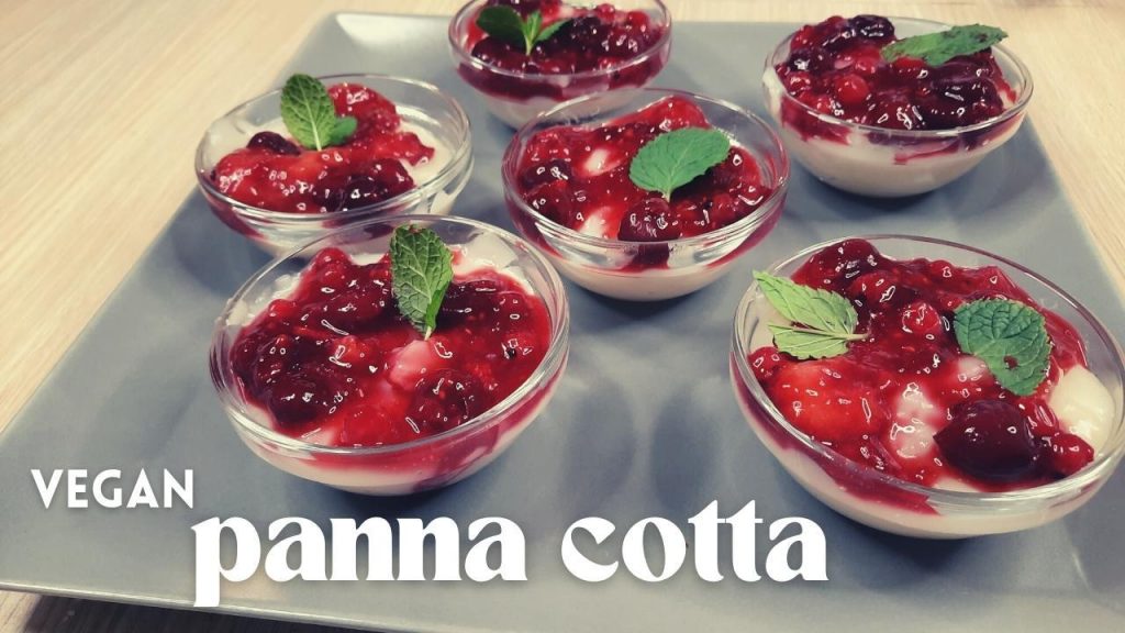 A square plate holds six small bowls of creamy vegan panna cotta, each topped with berry sauce and mint leaves. In the bottom left corner, the words "Vegan Panna Cotta" elegantly accentuate this delightful dessert display.