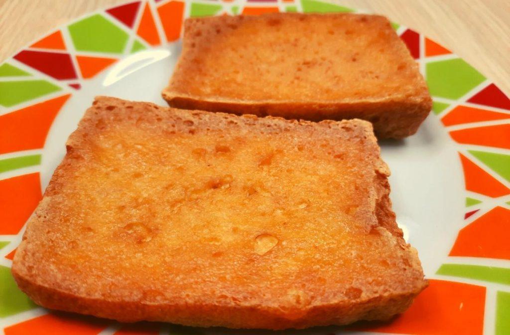 Aburaage Recipe ( Japanese Deep Fried Tofu) Two slices of toasted bread on a colorful plate with orange and green geometric patterns evoke the warmth of an aburaage recipe. The toast, golden brown, sits side by side on a light wooden surface.