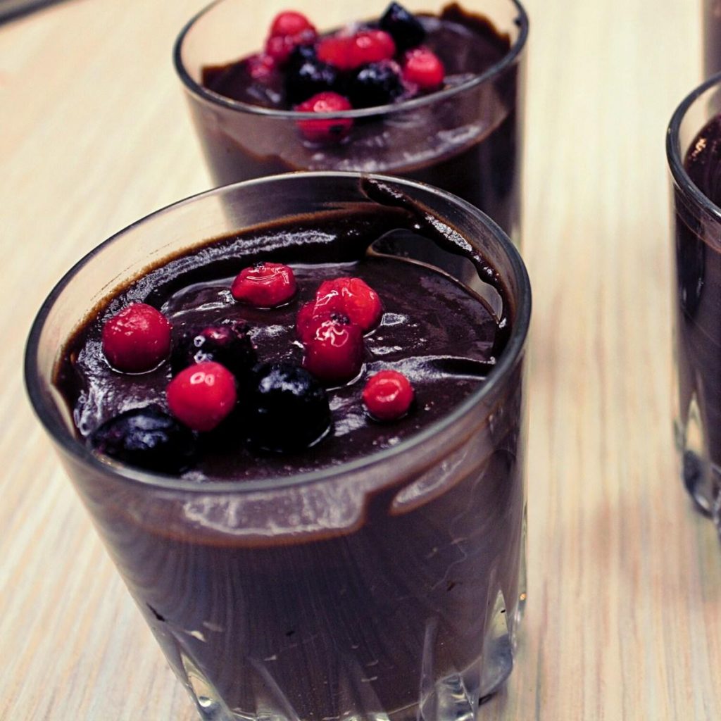 5-Ingredient Avocado Chocolate Mousse (Delicious and Nutritious Dessert) Glass cups filled with creamy avocado chocolate mousse, topped with fresh red and black berries, displayed on a light wooden surface.