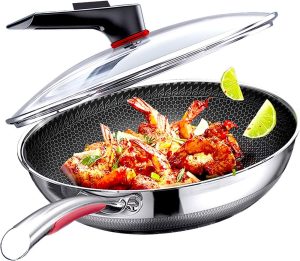 A stainless steel frying wok pan with a glass lid contains cooked shrimp garnished with herbs. Lime wedges adorn the rim for decoration. The pan features a textured non-stick surface and a sleek handle, making it an essential piece of kitchenware.
