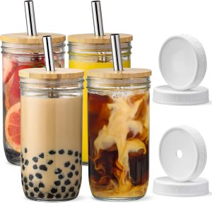 Four Mason jars with bamboo lids and stainless steel straws are filled with various drinks and ingredients like fruit slices, bubble tea, and swirling cream in coffee. Two spare white lids are placed beside the jars, adding to the practical elegance of these versatile glass cups.
