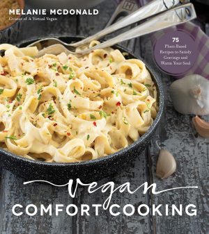 Vegan Comfort Cooking" by Melanie McDonald is a delightful cookbook showcasing plant-based recipes, with a creamy pasta dish gracing the cover. Garlic cloves in the backdrop and a text bubble promise "75 Recipes to Satisfy Cravings and Warm Your Soul.