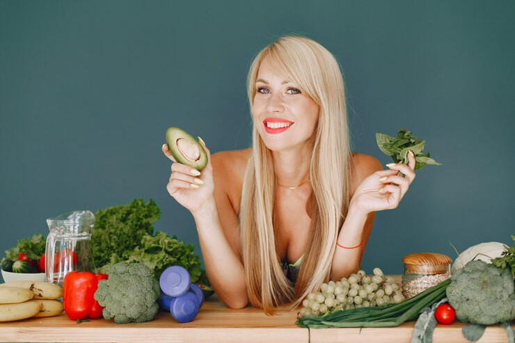 A woman holds an avocado alongside a variety of fresh vegetables, showcasing a healthy lifestyle and vibrant colors.
