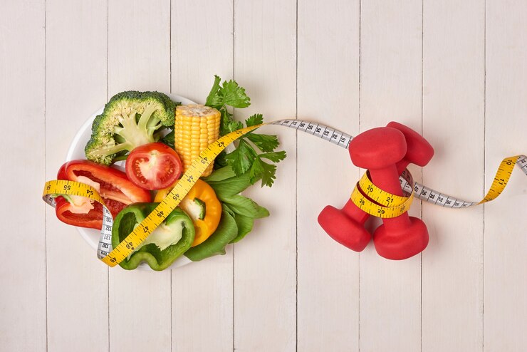 Lose Weight Naturally with the Paleo Vegan Diet "Plate of fresh vegetables, including bell peppers, broccoli, cucumber, and corn, with a measuring tape wrapped around them, symbolizing healthy eating for weight loss. Next to the plate are red dumbbells also wrapped with a measuring tape, representing fitness and weight management."