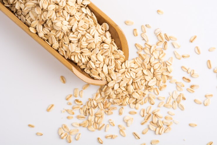 "Wooden scoop overflowing with raw oats on a white background, with oats scattered around, symbolizing a healthy and nutritious whole grain option."