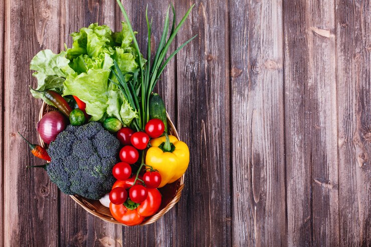 Fresh vegetables arranged in a wooden bowl, resting on a rustic wooden table, showcasing vibrant colors and textures. The natural setting highlights the freshness of the produce.