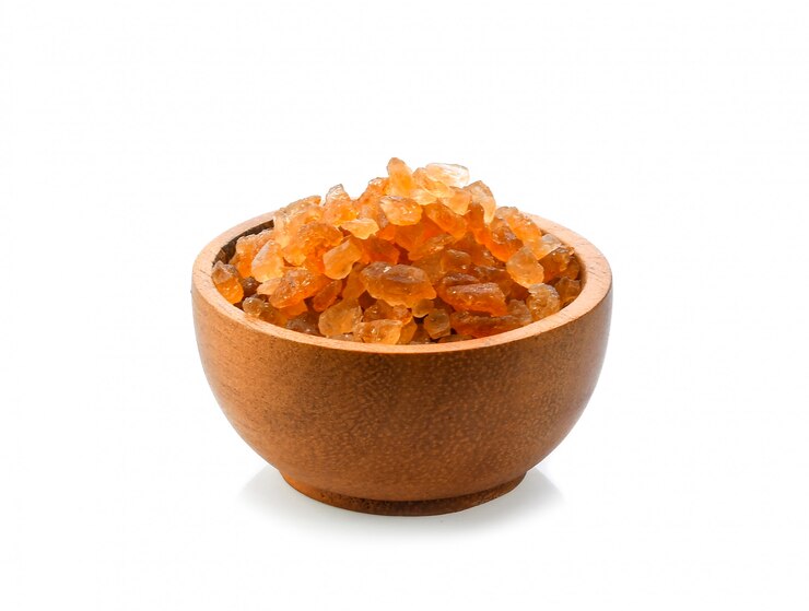 A wooden bowl filled with peach gums, placed on a wooden surface. The peach gum pieces are large, crystalline, and have a slightly translucent appearance, highlighting their texture and natural beauty.