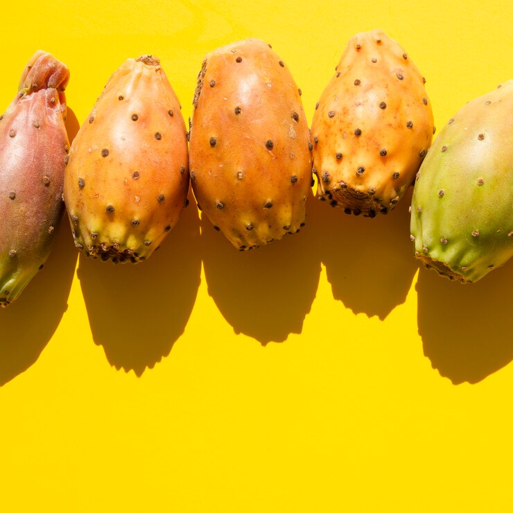 A top-view shot of a variety of prickly pears arranged in a circular frame on a yellow background. The colorful assortment includes spiny fruits creating a vibrant and appetizing display.