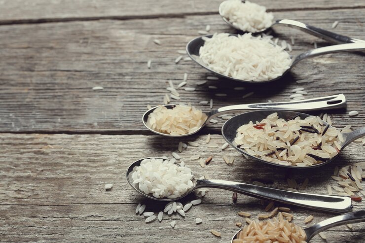An assortment of various types of rice displayed on a wooden table. The different grains, including white, brown, and wild rice, highlight the diversity in texture and color.