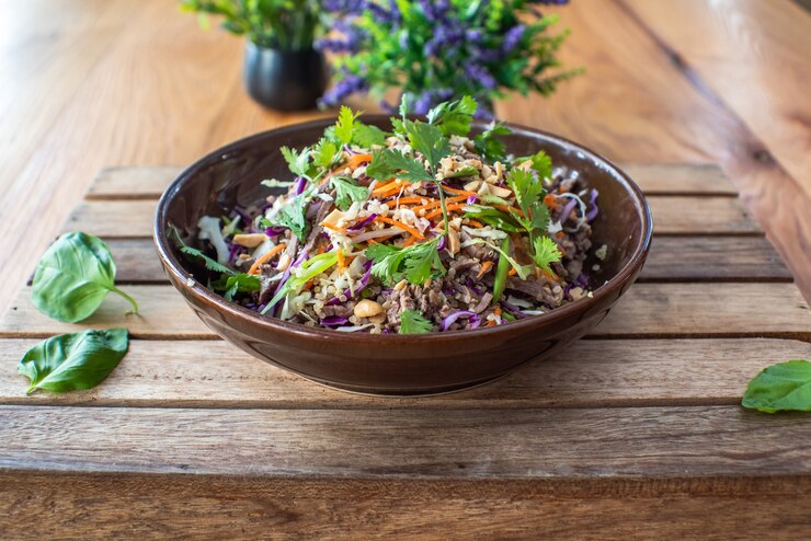 A bowl of Sweetgreen Style Crispy Rice Salad filled with fresh vegetables and herbs, placed on a rustic wooden table.