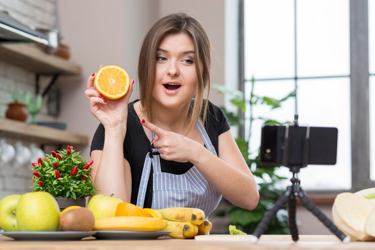 A woman captures a photo while holding an orange, representing the vibrant plant-based lifestyle of vegan influencers.
