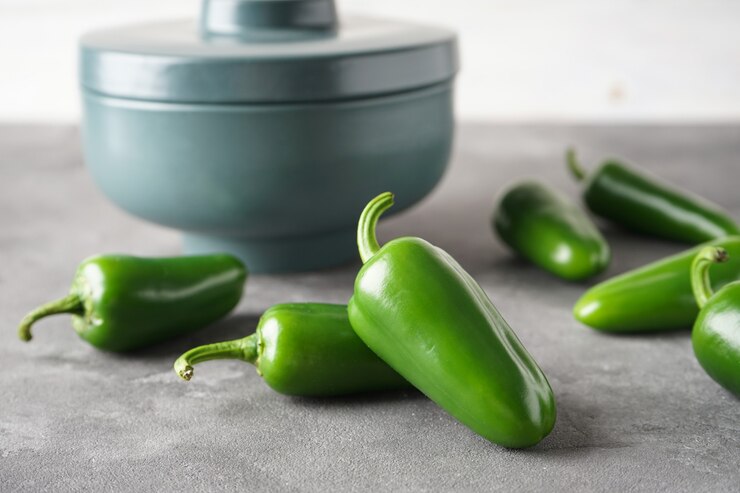 Fresh green jalapenos displayed on a grey background, highlighting their vibrant color and texture for culinary use.