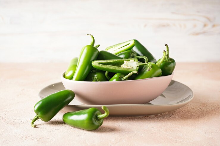 A bowl filled with vibrant green jalapenos placed on a wooden table, showcasing their fresh appearance.