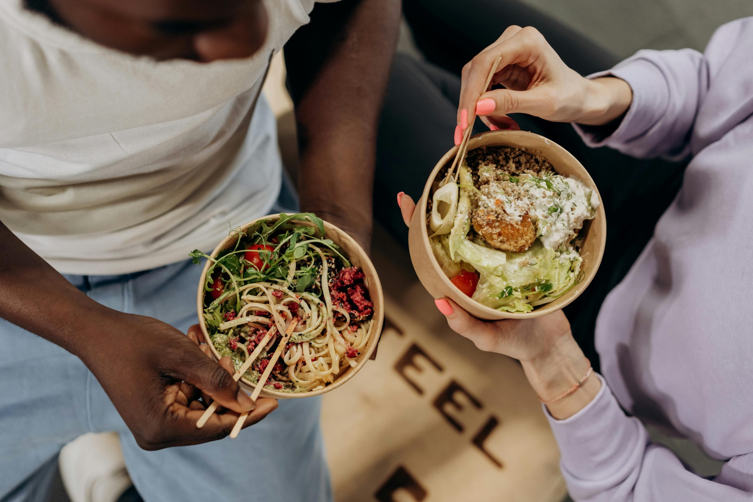 A couple sits on a couch, holding bowls of crispy rice salad, enjoying a popular TikTok recipe in a relaxed setting.