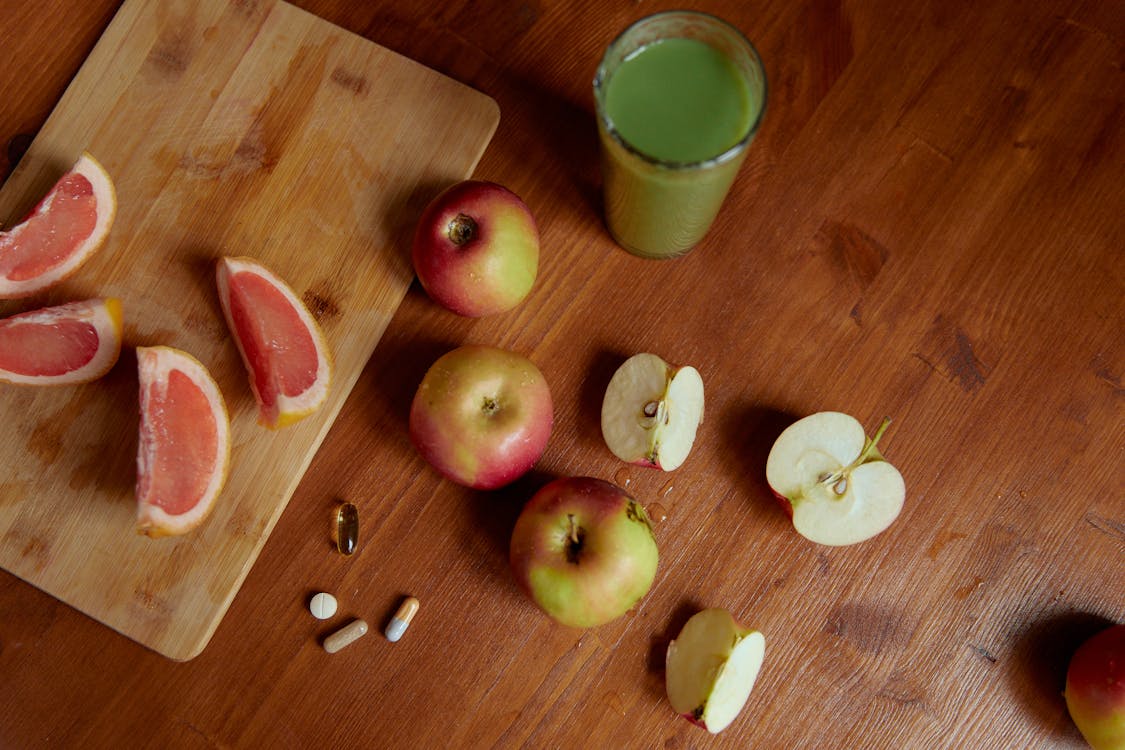 Fresh apples, supplements, and a glass of juice rest on a wooden cutting board, highlighting a vegan approach to weight loss.