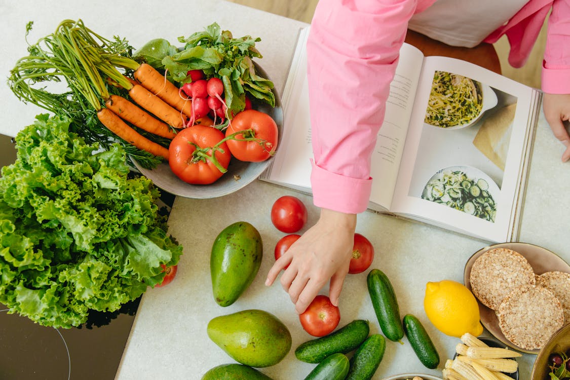 A woman is chopping fresh vegetables and arranging colorful fruits while preparing a healthy meal in her kitchen.