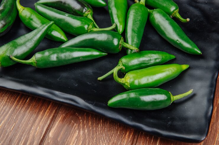 A black plate featuring fresh jalapenos, vibrant green peppers ready for consumption.