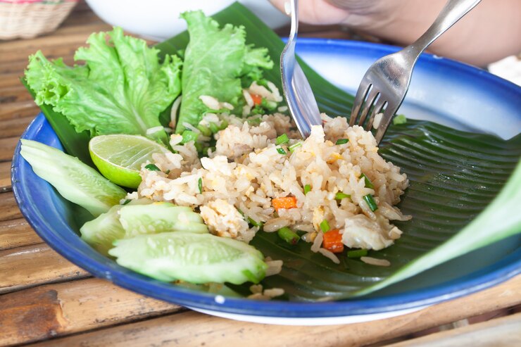 A bowl of traditional Laotian crispy rice salad with vegetables, garnished with herbs and a fork resting beside it.