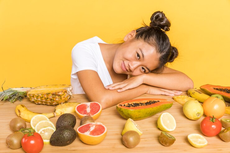 A girl smiles joyfully, surrounded by a vibrant array of fresh fruits, symbolizing the benefits of a vegan diet for detoxification.