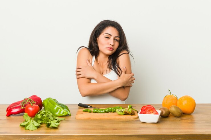 A woman sits at a table filled with fresh vegetables and fruits, promoting a vegan diet for eczema relief.