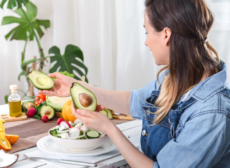 A woman enjoys an avocado and assorted fruits, highlighting the benefits of a vegan diet for digestive health.