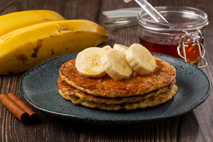 A stack of vegan banana oat pancakes topped with sliced bananas and a sprinkle of cinnamon.