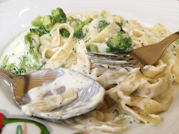 A plate of creamy vegan Alfredo fettuccine with broccoli, accompanied by a fork, perfect for a romantic Valentine's Day meal.