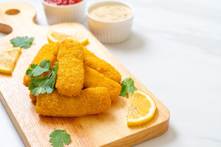 Cheesy vegan mozzarella sticks with lemon slices on a wooden cutting board, perfect for Valentine's Day.