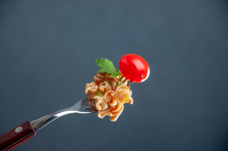 A fork holding a small piece of vegan tomato fusilli pasta topped with a cherry, perfect for Valentine's Day.