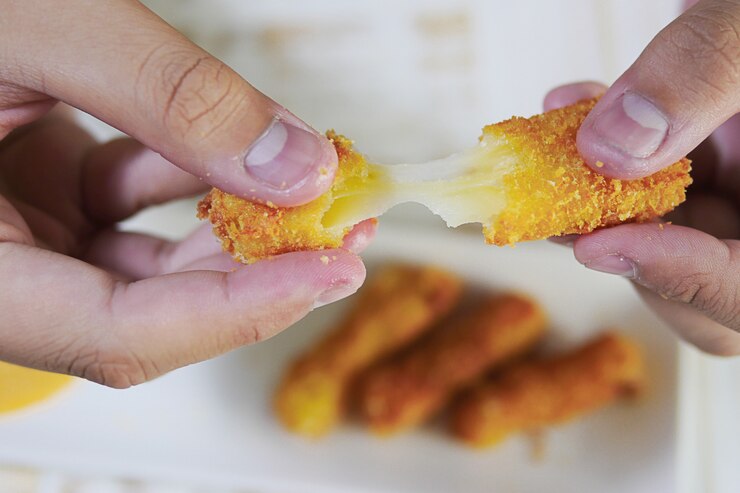 A hand presents a delicious serving of cheesy vegan mozzarella sticks, ideal for sharing on Valentine's Day.